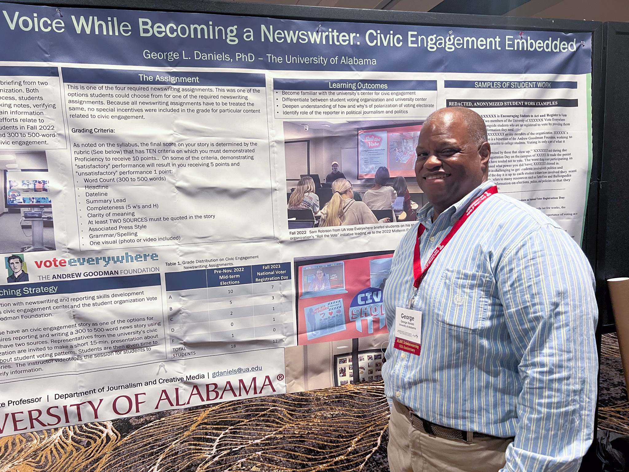 Dr. George Daniels poses in front of his work at AEJMC 2024 in Philadelphia, Pennsylvania.