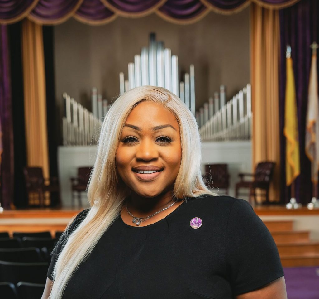 Candice Hardy standing in an auditorium with a pipe organ in the background on the stage.